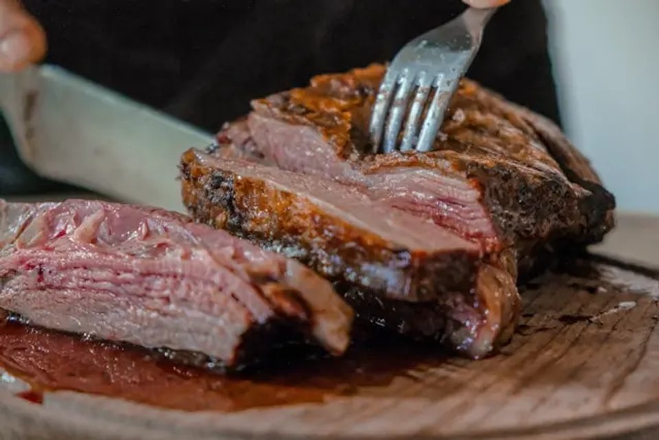 A close-up of a perfectly cooked brisket being sliced with a fork and knife, showcasing its juicy texture and rich color on a wooden cutting board.