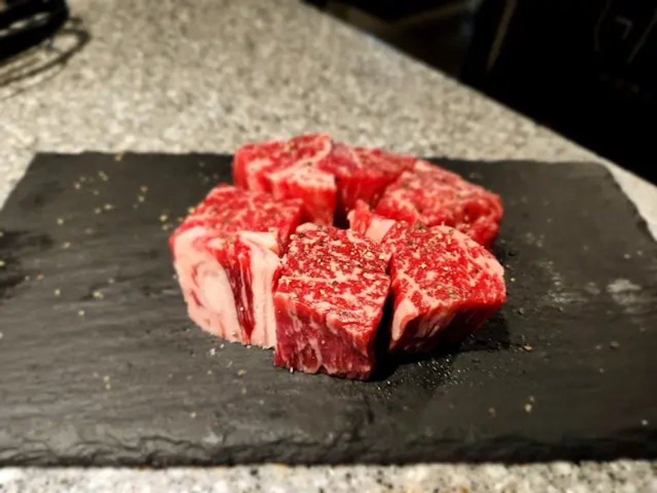 A selection of premium beef cuts seasoned with spices, arranged on a black slate surface.